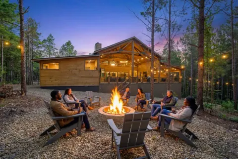 The Avalon, an example cabin listed by Beavers Bend Cabin Country, with a covered deck and fire pit among pine trees