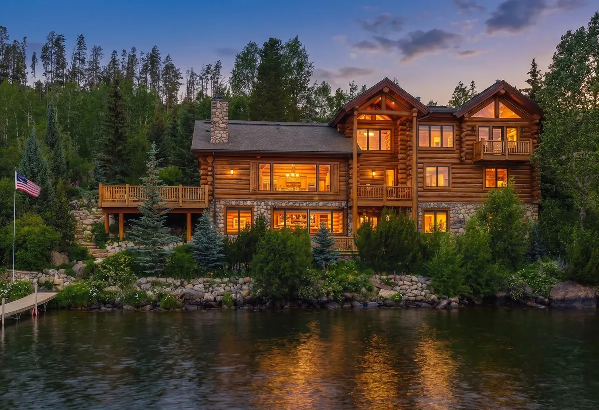 Grand Lincoln Log Cabin glowing at dusk beside Grand Lake, an example Grand Mountain Rentals cabin