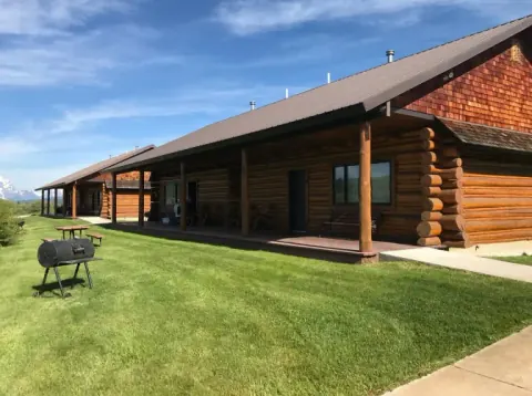Row of Teton Cabins log cabins with covered porches along a green lawn