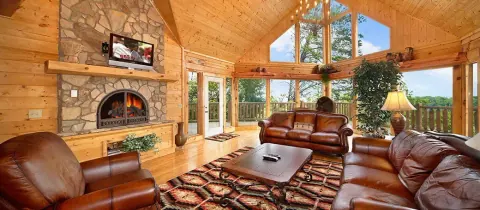 Log-cabin living room with a stone fireplace and wooded mountain view, from the Cabins USA family cabin collection